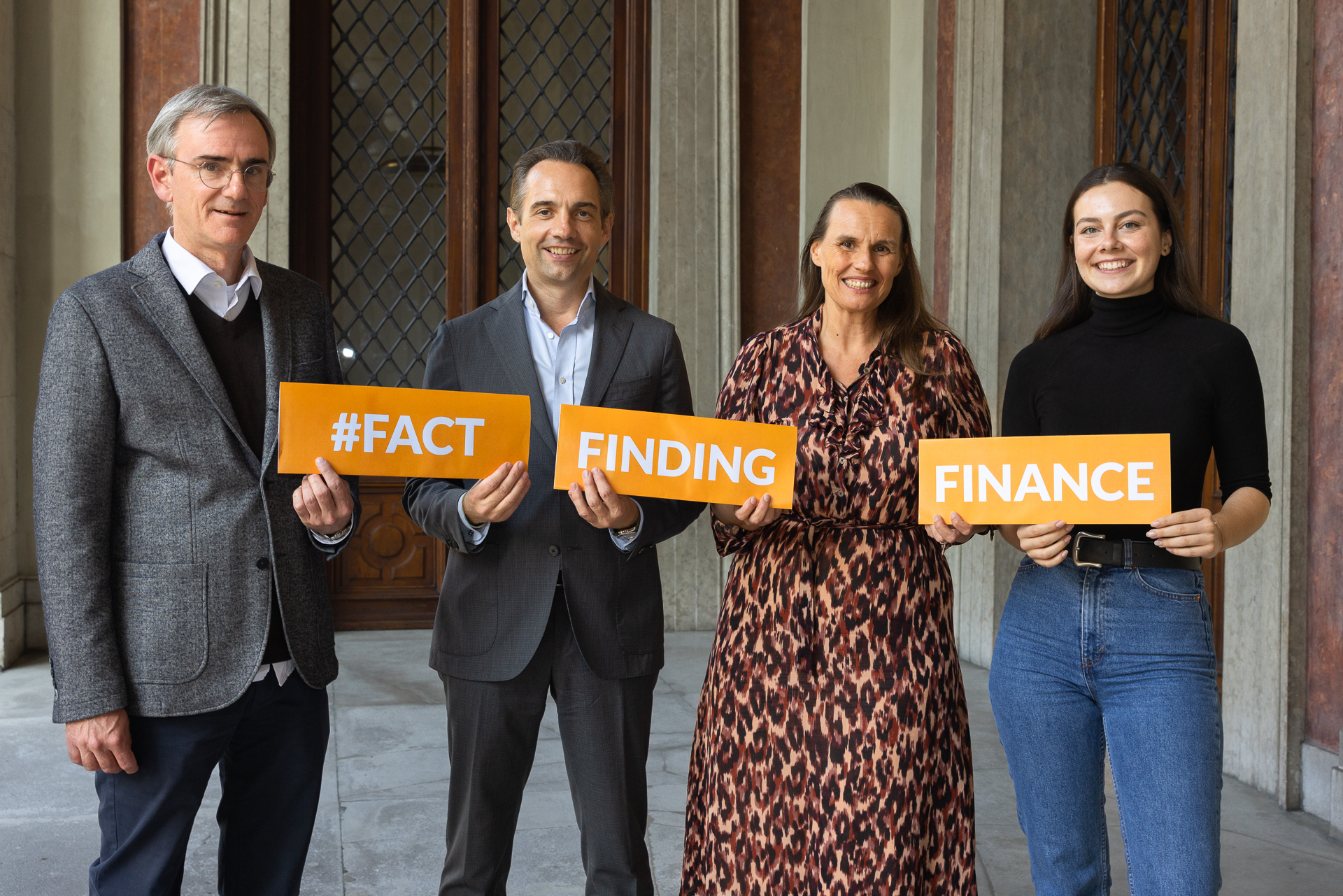 Vier Personen die gemeinsam 3 Schilder hochhalten die zusammen das Wort „#Fact Finding Finance“ ergeben.
